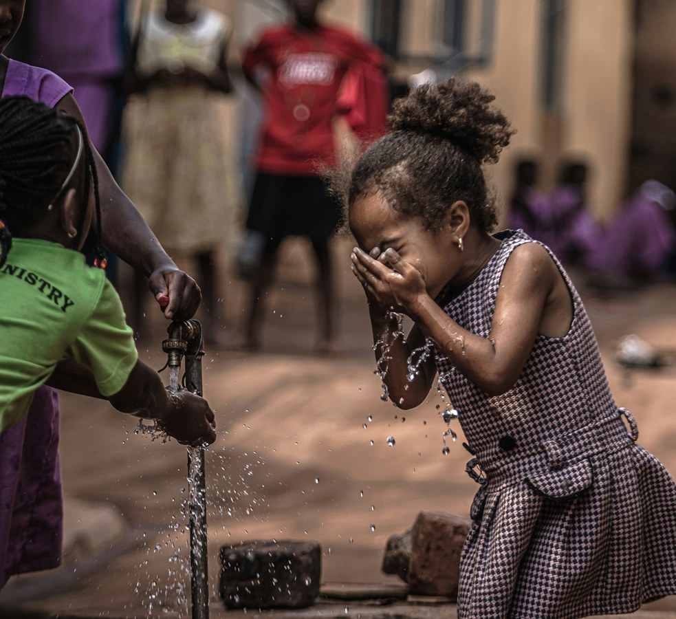 A young girl drinking fresh water from her hands beside a community tap.