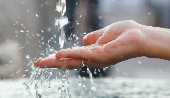 Cupped hands catching clear water as it falls from a standpipe.