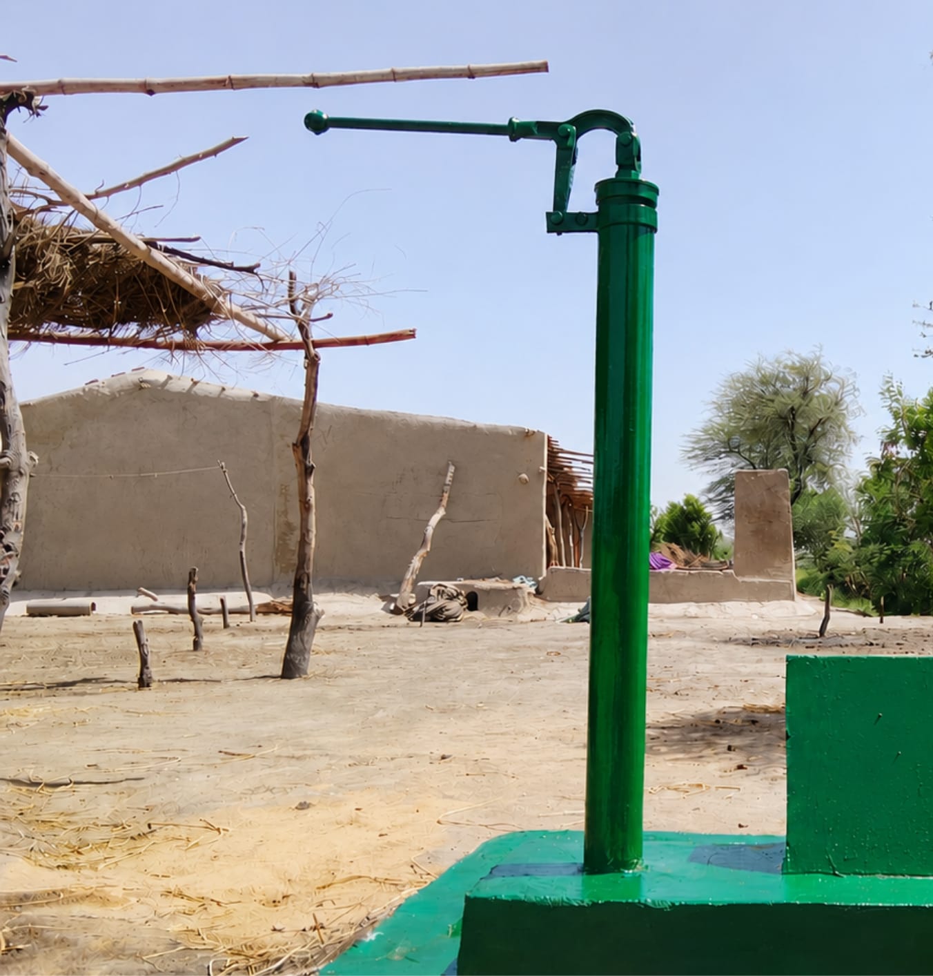 A newly installed green hand pump standing on a painted plinth in a village courtyard.